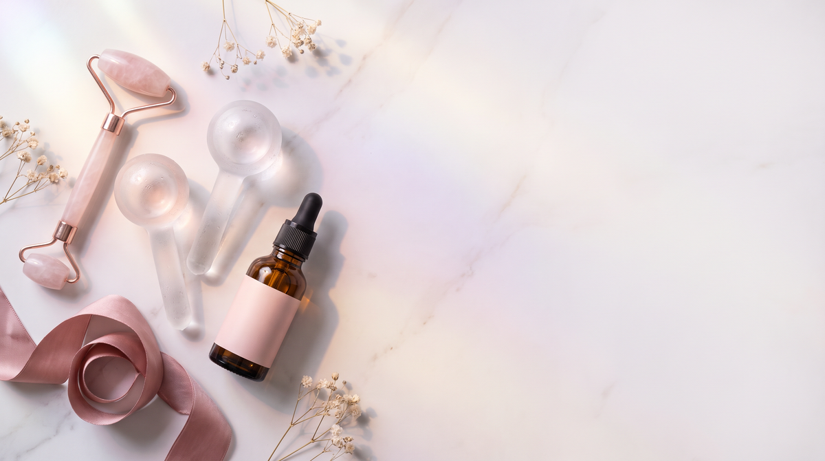Aurora Ritual hero — rose quartz roller, ice globes, and serum on marble with holographic light